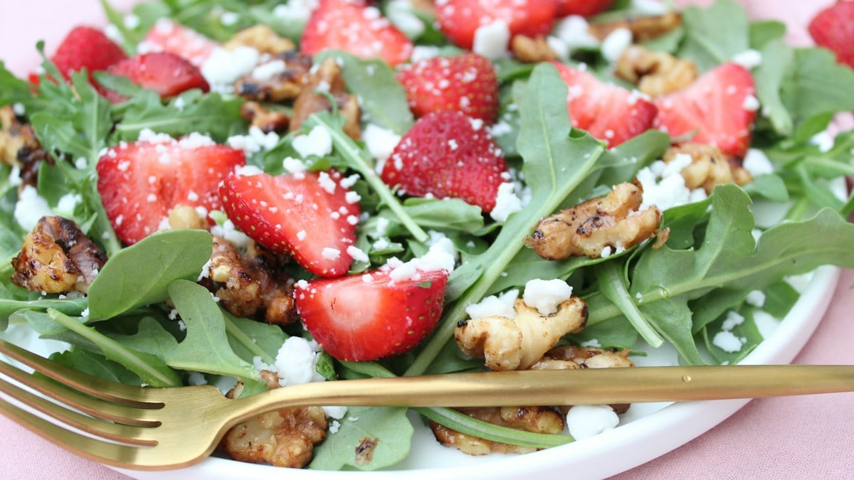 A white plate topped with a salad covered in strawberries
